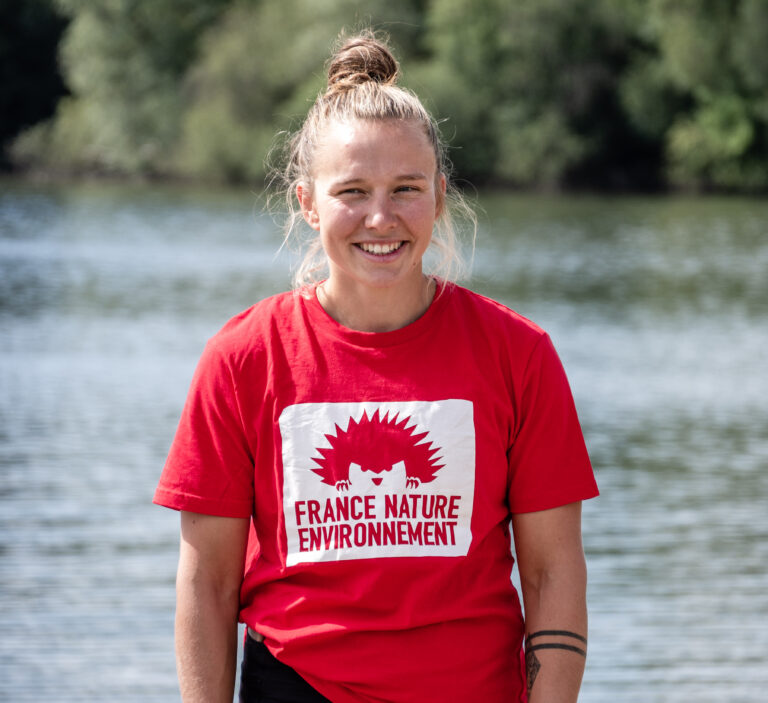 Portait d'une femme blonde avec un tshirt rouge FNE devant un plan d'eau