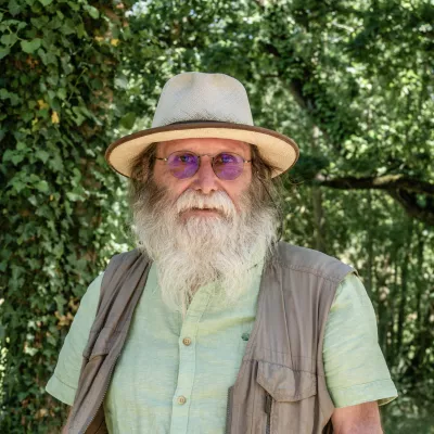 homme blanc avec lunette et chapeau barbe blanche arriere plan boisé