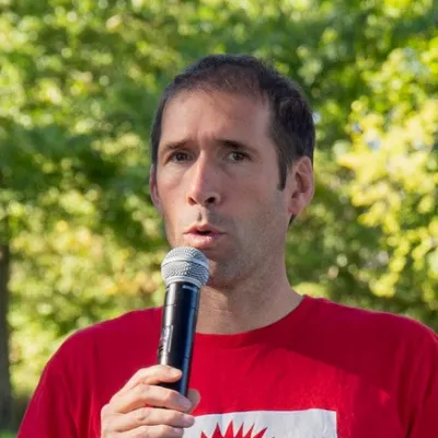 Xavier debout en train de parler au micro avec un t-shirt rouge FNE